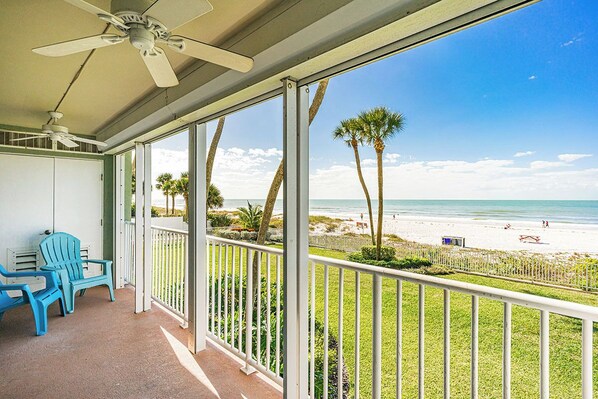A balcony with a view of the beach, a ceiling fan, and two blue chairs. - Sand Castle I 202 - GULF FRONT Condo! (Indian Shores)