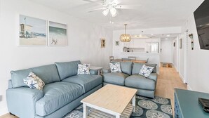 Un salon moderne avec un canapé d’angle, une table basse en bois et un ventilateur de plafond.