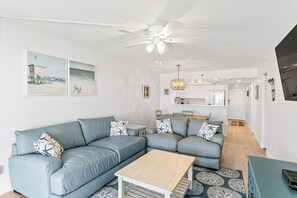 A modern living room with a sectional sofa, a wooden coffee table, and a ceiling fan. - Sand Castle I 202 - GULF FRONT Condo! (Indian Shores)