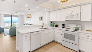 Une cuisine moderne avec des meubles blancs, un îlot central, un four encastré et un four à micro-ondes.