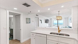 A modern kitchen with white cabinetry, a dishwasher, and a large window with a view of the outdoors.