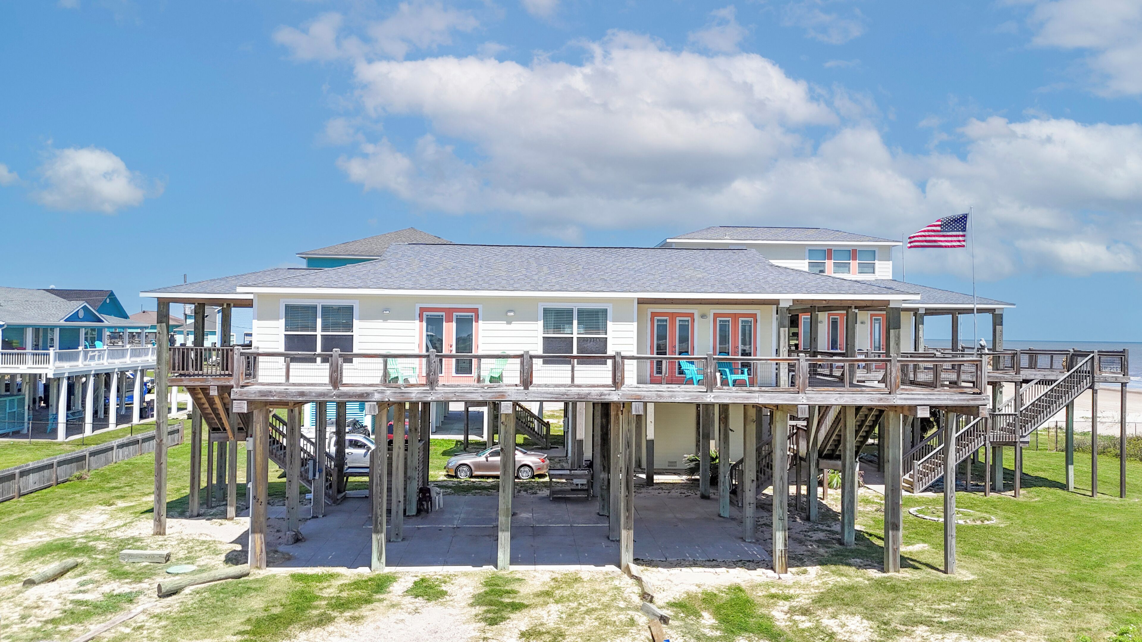 Une maison située en bord de mer, dotée d’une terrasse en bois, d’un drapeau et offrant une vue sur l’océan.