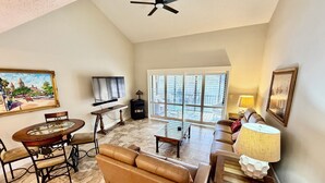 A living room with a sofa, a coffee table, a TV, and a painting on the wall. - Soak up the Florida sunshine in this modern Gold-rated condo overlooking the lagoon and pool. (Saint Augustine)