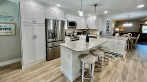 A modern kitchen with white cabinetry, stainless steel appliances, and a central island with bar stools.