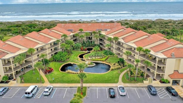 A hotel with a central courtyard featuring a pond, surrounded by lush greenery and palm trees. The building has a red-tiled roof and multiple balconies.