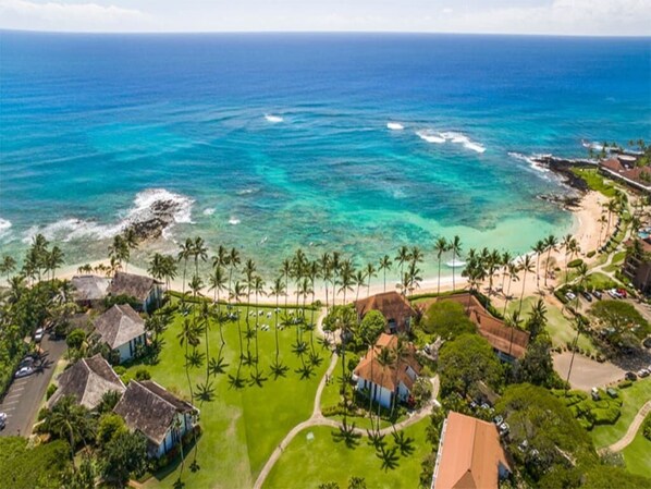 An aerial view of a coastal resort with beachfront properties, palm trees, and ocean views.