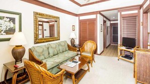 Un salon comprenant un canapé, deux fauteuils en osier, une table basse, un téléviseur posé sur un meuble et un ventilateur de plafond.