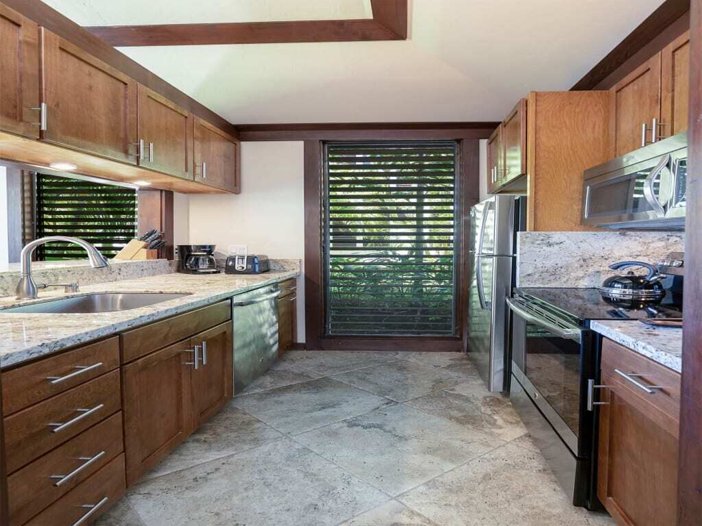 Una cocina con armarios de madera, un refrigerador de acero inoxidable y una ventana con persianas.