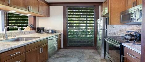 Una cocina con armarios de madera, un refrigerador de acero inoxidable y una ventana con persianas.