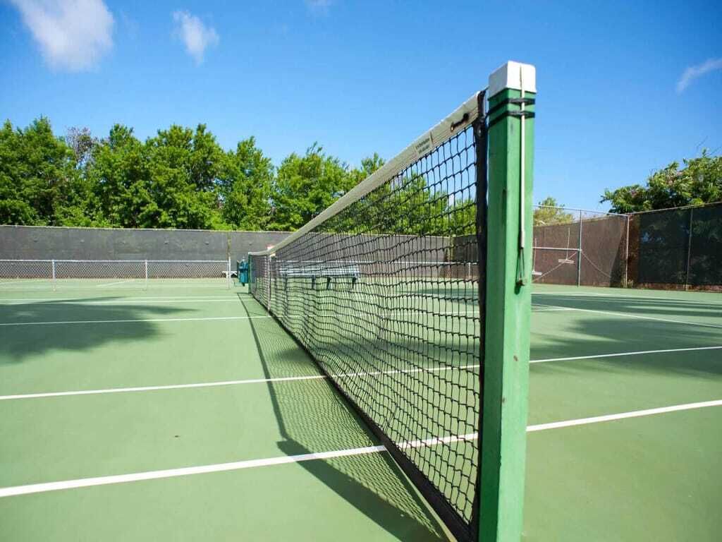 Una cancha de tenis con red, superficie verde y líneas delimitadoras blancas.