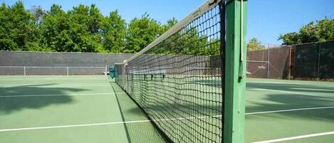 Una cancha de tenis con red, superficie verde y líneas delimitadoras blancas.