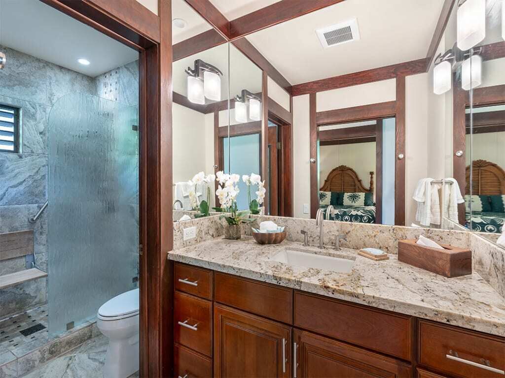 A bathroom with a marble countertop, wooden cabinets, a large mirror, and a shower area.