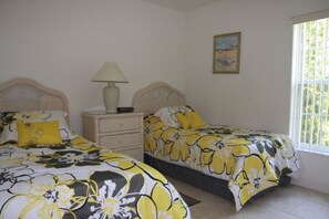 Une chambre avec deux lits, une table de chevet, une lampe et une fenêtre avec des stores.