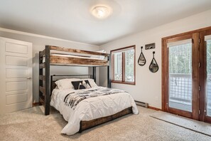 A bedroom with a bunk bed, a large window, and a door with a view of trees.