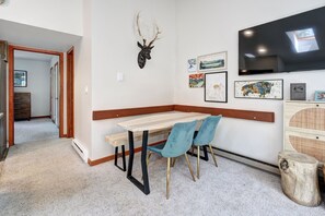 A room with a wooden bench, two blue chairs, a mounted deer head, and framed artwork on the wall.
