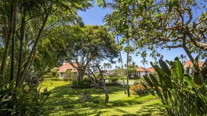 A lush garden with a pathway leading to a building with a red roof. - Comforts of Home+Lanai to Lawn, WiFi, Flat Screen, Kitchen–Kiahuna Plantation #2065 (KOLOA)