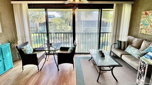 A room with a ceiling fan, a sofa, a dining table, and a chair. There is a view through large windows to the outside. - Cozy Silver-rated condo, perfect for enjoying beautiful Florida. (Saint Augustine)