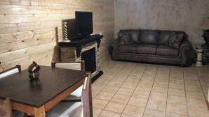 Um quarto com painéis de madeira, lareira, sofá e mesa de jantar.