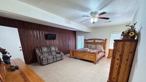 Um quarto espaçoso com uma cama de madeira, um sofá, uma mesa de madeira e um ventilador de teto.