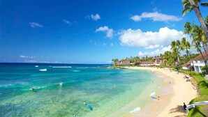 Una playa con aguas turquesas cristalinas, palmeras y un resort con edificios a lo largo de la costa.