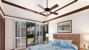 Un dormitorio con una cama, ventilador de techo, mesita de noche y ventana con persianas.