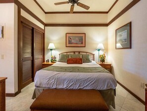 A neatly arranged bedroom with a bed, bedside lamps, a ceiling fan, and a framed picture on the wall. - Upgraded Condo w/Lanai to Lawn, Modern Kitchen+Bath, WiFi–Kiahuna Plantation #2045 (KOLOA)