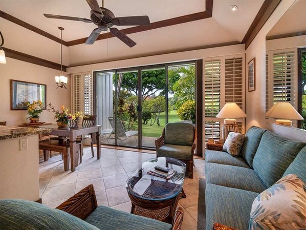 A spacious living area with a ceiling fan, a dining table, a sofa, and a large sliding glass door leading to a garden. - Upgraded Condo w/Lanai to Lawn, Modern Kitchen+Bath, WiFi–Kiahuna Plantation #2045 (KOLOA)