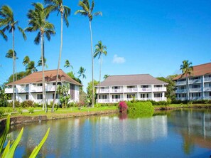 A hotel with a large pond, palm trees, and a clear blue sky. - Upgraded Condo w/Lanai to Lawn, Modern Kitchen+Bath, WiFi–Kiahuna Plantation #2045 (KOLOA)