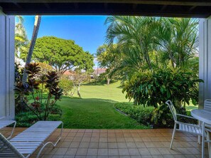 A patio with a view of a well-maintained lawn and palm trees. - Upgraded Condo w/Lanai to Lawn, Modern Kitchen+Bath, WiFi–Kiahuna Plantation #2045 (KOLOA)