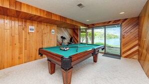 Una mesa de billar en una sala con paneles de madera y vistas a un lago.