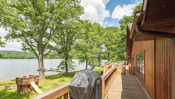 Una terraza de madera con una parrilla, un tobogán y vistas a un lago y árboles.