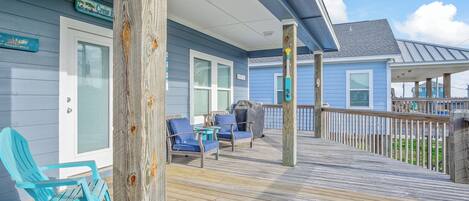 A wooden deck with outdoor seating, a covered area, and a view of the ocean.