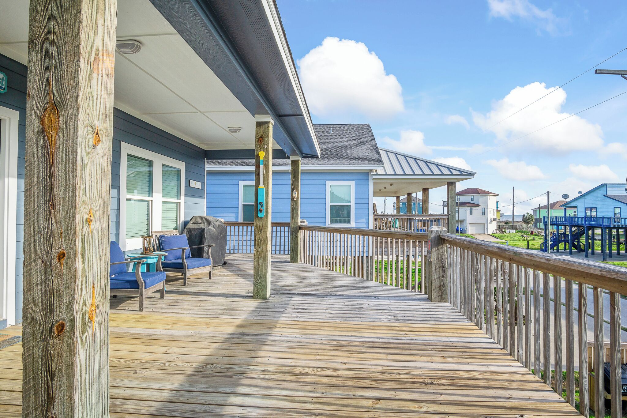 A wooden deck with outdoor furniture, a covered area, and a view of neighboring houses.