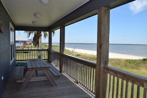 Une véranda couverte, avec une table en bois et des bancs, donnant sur une plage et l’océan.