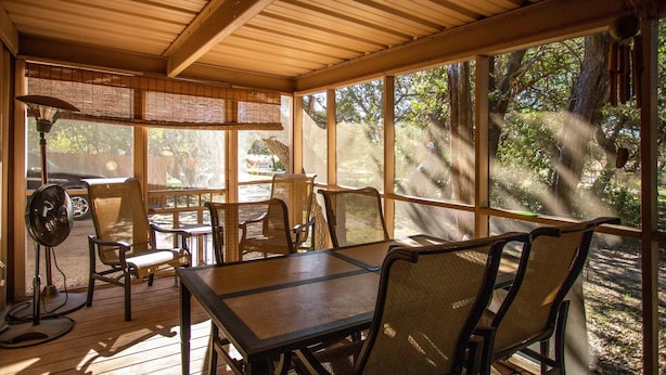 Un espacio al aire libre techado con mesa y sillas, ventanas amplias y un ventilador.