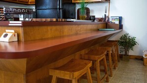 Una barra de madera con taburetes, un refrigerador negro y una planta en maceta.