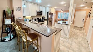 A modern kitchen with white cabinets, a large island, stainless steel appliances, and pendant lighting. - Perfect family Gold-rated condo with easy access to pool and beach! (Saint Augustine)