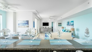 Una cocina moderna con encimera de granito, un comedor con mesa para cuatro personas y una sala de estar con sofá y televisor.