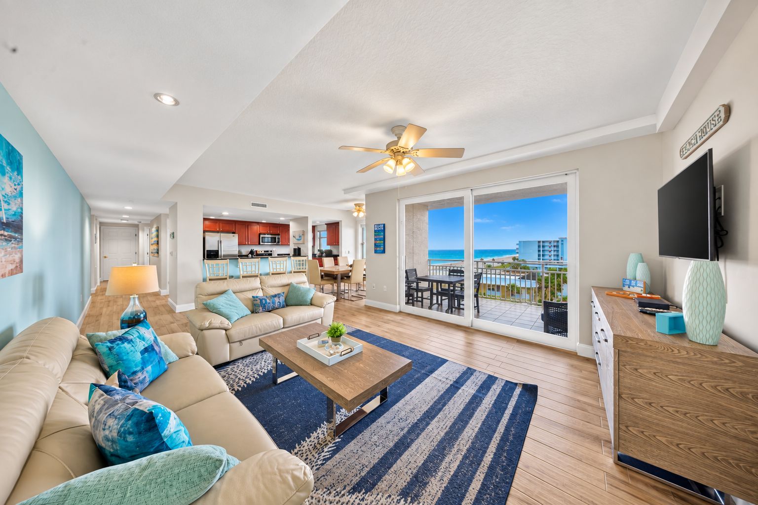 A modern living room with a sofa, coffee table, and a view of the beach through large sliding doors.