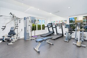 Un gimnasio con máquinas de cardio, equipo de levantamiento de pesas y una banca.