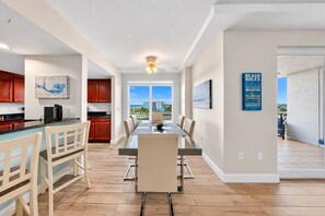 A modern kitchen with wooden cabinets, a dining area with a glass table, and a view of the beach.