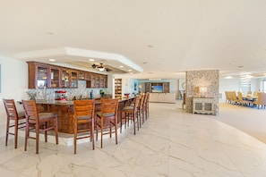 A spacious kitchen with a bar area, wooden chairs, and a dining table.