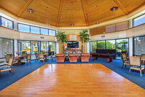 Un espacio interior amplio con piso de madera, diversas opciones de asientos y ventanas grandes que ofrecen vistas al exterior.