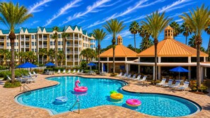 A hotel pool area with multiple lounge chairs, a swimming pool, and palm trees. - Harbour Village 2304 | Golf/Tennis/Pool | River View (Ponce Inlet)