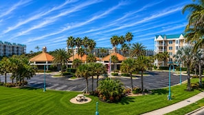 A hotel with a parking lot, palm trees, and a clear blue sky. - Harbour Village 2304 | Golf/Tennis/Pool | River View (Ponce Inlet)
