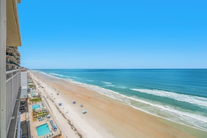 Vue sur la plage depuis un immeuble de grande hauteur, avec une piscine et des parasols de plage.