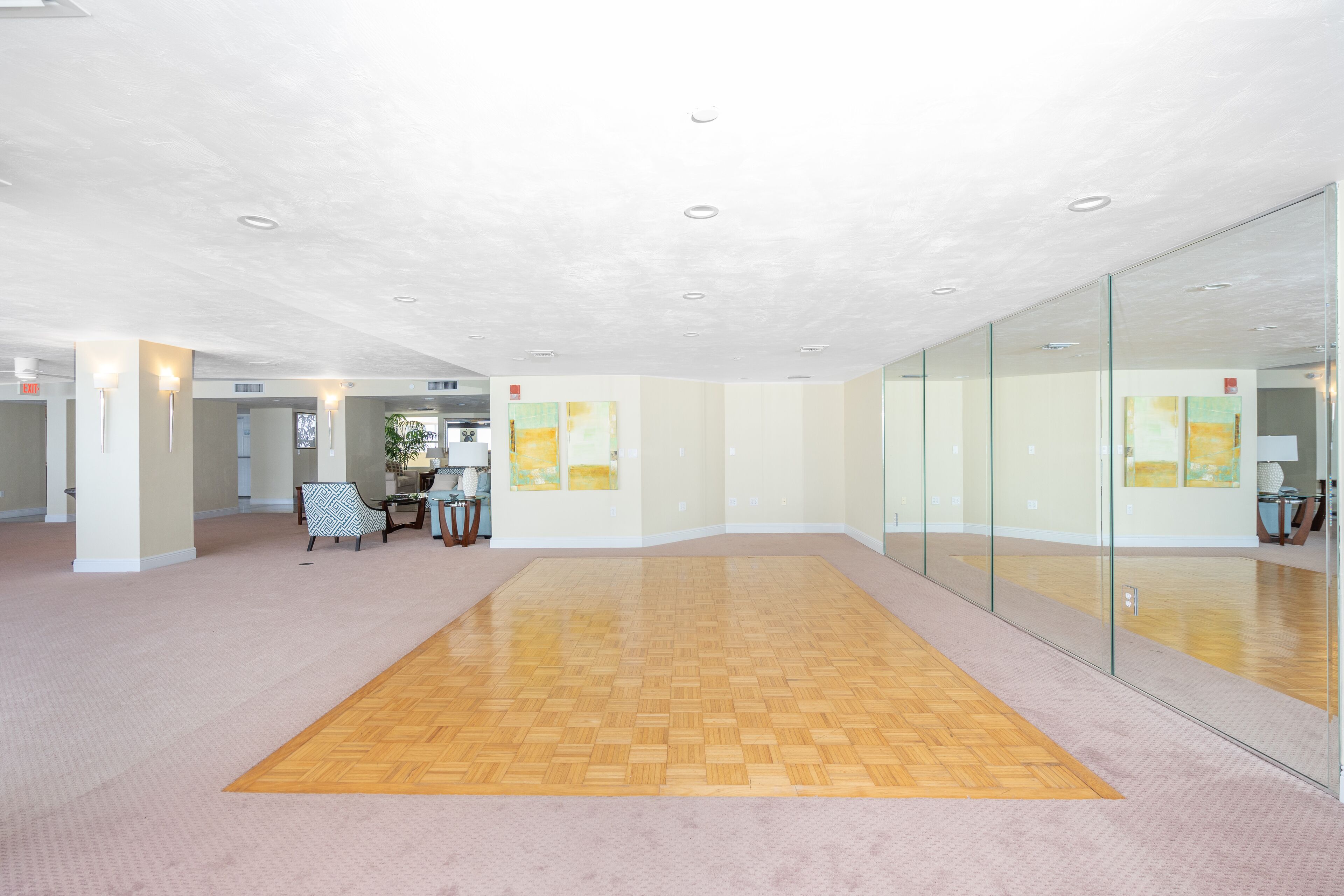 A spacious lobby with a wooden parquet floor, glass walls, and a few pieces of furniture.