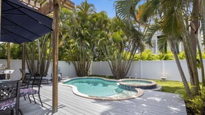 A backyard with a swimming pool, wooden deck, outdoor furniture, and palm trees. - Havana Cay- Adorable 3 bedroom cottage style- Pool/spa and only 4 houses from be (Anna Maria)