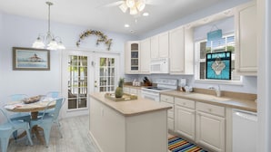 A kitchen with white cabinets, a central island, and a dining area with blue chairs. - Havana Cay- Adorable 3 bedroom cottage style- Pool/spa and only 4 houses from be (Anna Maria)