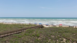 A beach with a wooden boardwalk leading to the shore, surrounded by sparse vegetation. - Suntide II 206 - Condo w/ Private Balcony, Beachfront Pool & Spa, Sun Deck, Sand Volleyball, Tennis Court (South Padre Island)